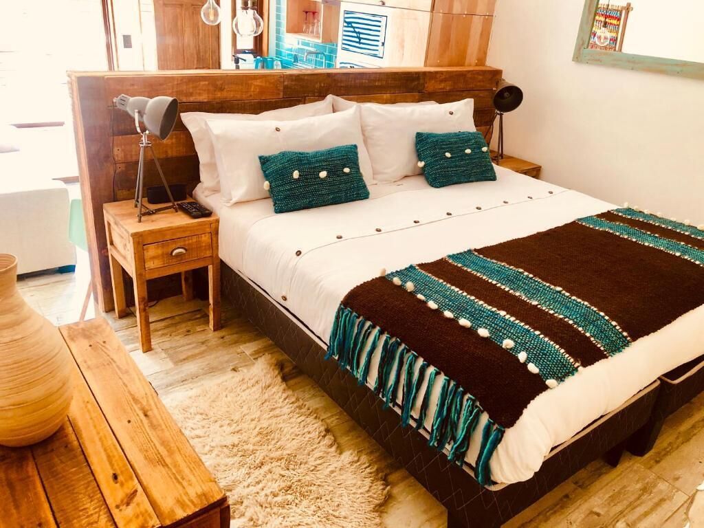 Quarto bem organizado com cabeceira de madeira, cama com almofadas brancas e azul-turquesa, manta listrada marrom e azul-turquesa, mesa de cabeceira de madeira e uma pequena mesa com um vaso.