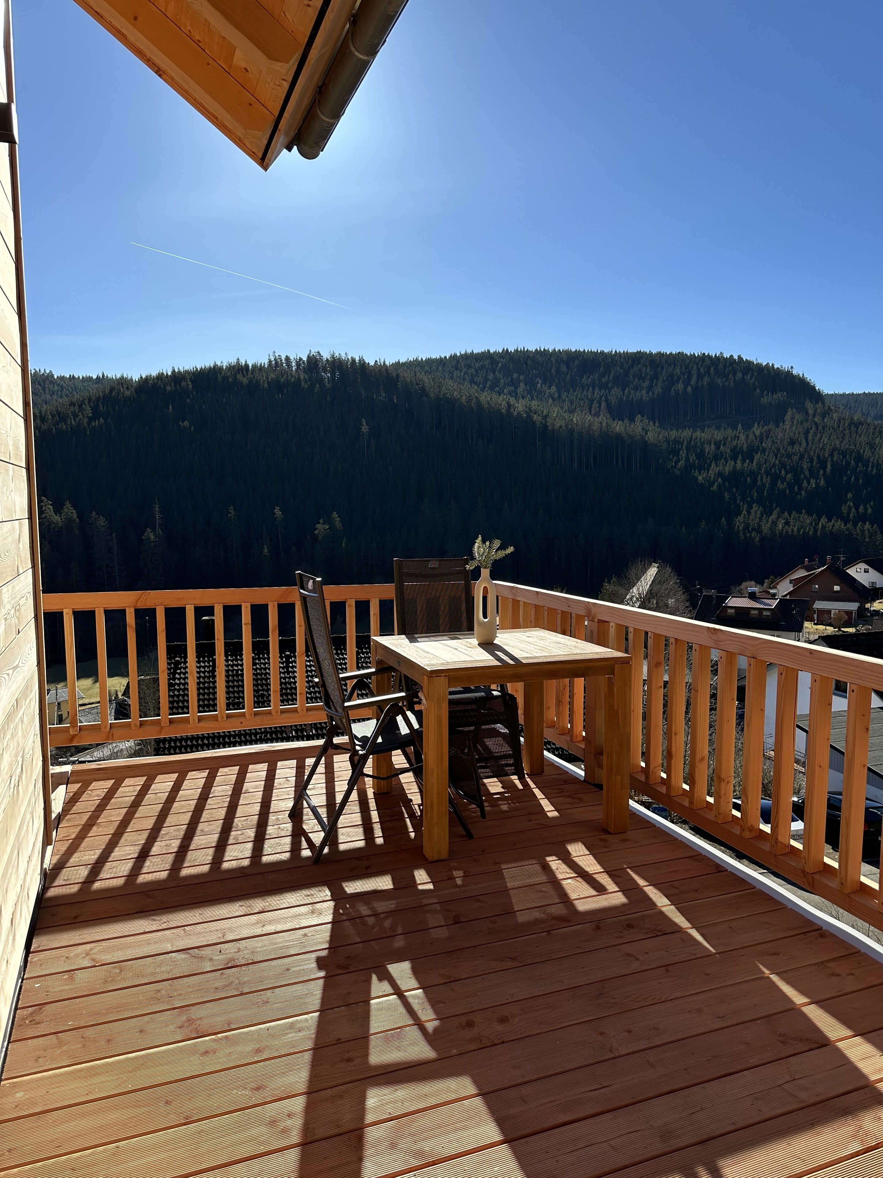 Una terraza de madera con una mesa y sillas, con vista a una montaña boscosa.