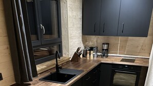 Una cocina moderna con piso de madera en espiga, armarios negros, horno integrado y pileta negra.