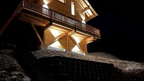 Una casa de madera con balcón, ventanas iluminadas y una escalera que lleva a ella.