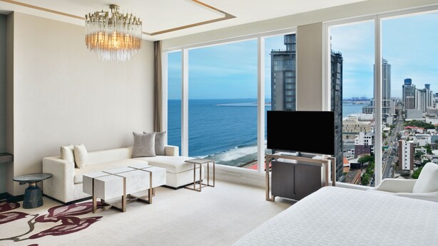A modern hotel room with a large window, a chandelier, a sofa, a TV, and a bed. - Sheraton Colombo Hotel (Colombo)