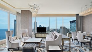 A modern hotel room with a large window offering a city view, a flat-screen TV, a sofa set, a dining table, and a patterned rug. - Sheraton Colombo Hotel (Colombo)