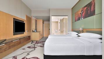 A hotel room with a bed, a TV, a bathroom, and a painting on the wall.