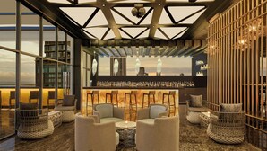 A modern bar area with seating, a high ceiling with geometric patterns, and a view of buildings through large windows. - Sheraton Colombo Hotel (Colombo)