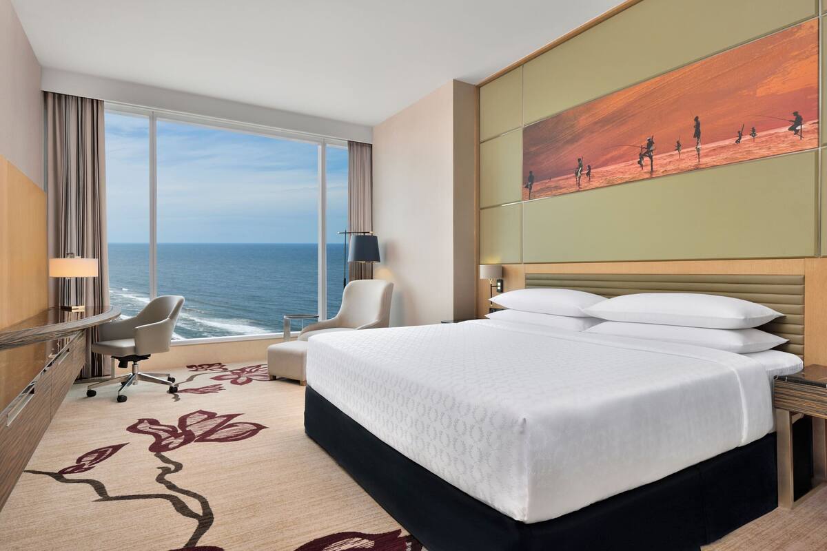 Habitación de hotel con una cama grande, un escritorio, una silla y vista al océano.