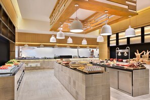 A modern kitchen with a central island, pendant lighting, and a variety of food items displayed.