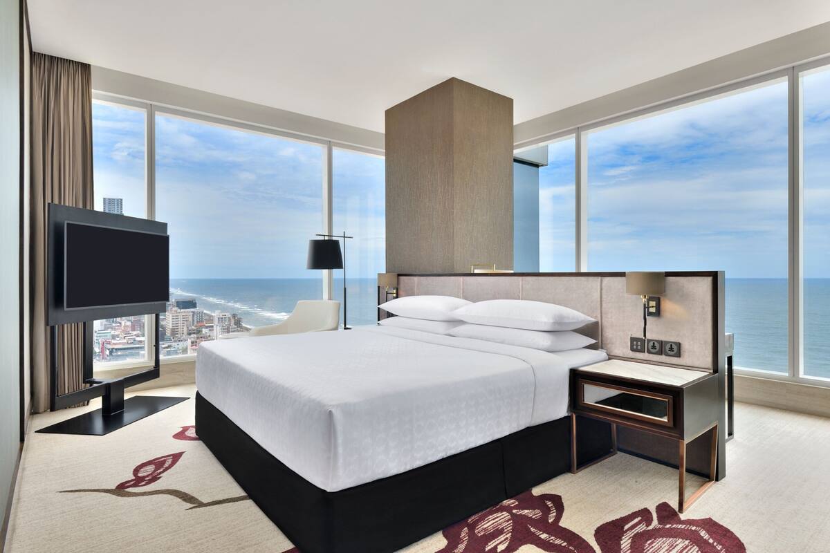 Habitación de hotel con una cama grande, televisión, mesita de noche y vistas al océano.