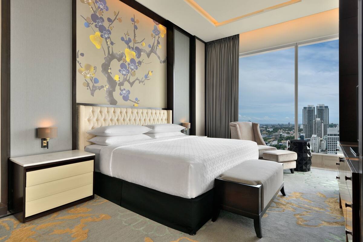 Habitación de hotel moderna con una cama grande, una silla, un escritorio y vistas a la ciudad.