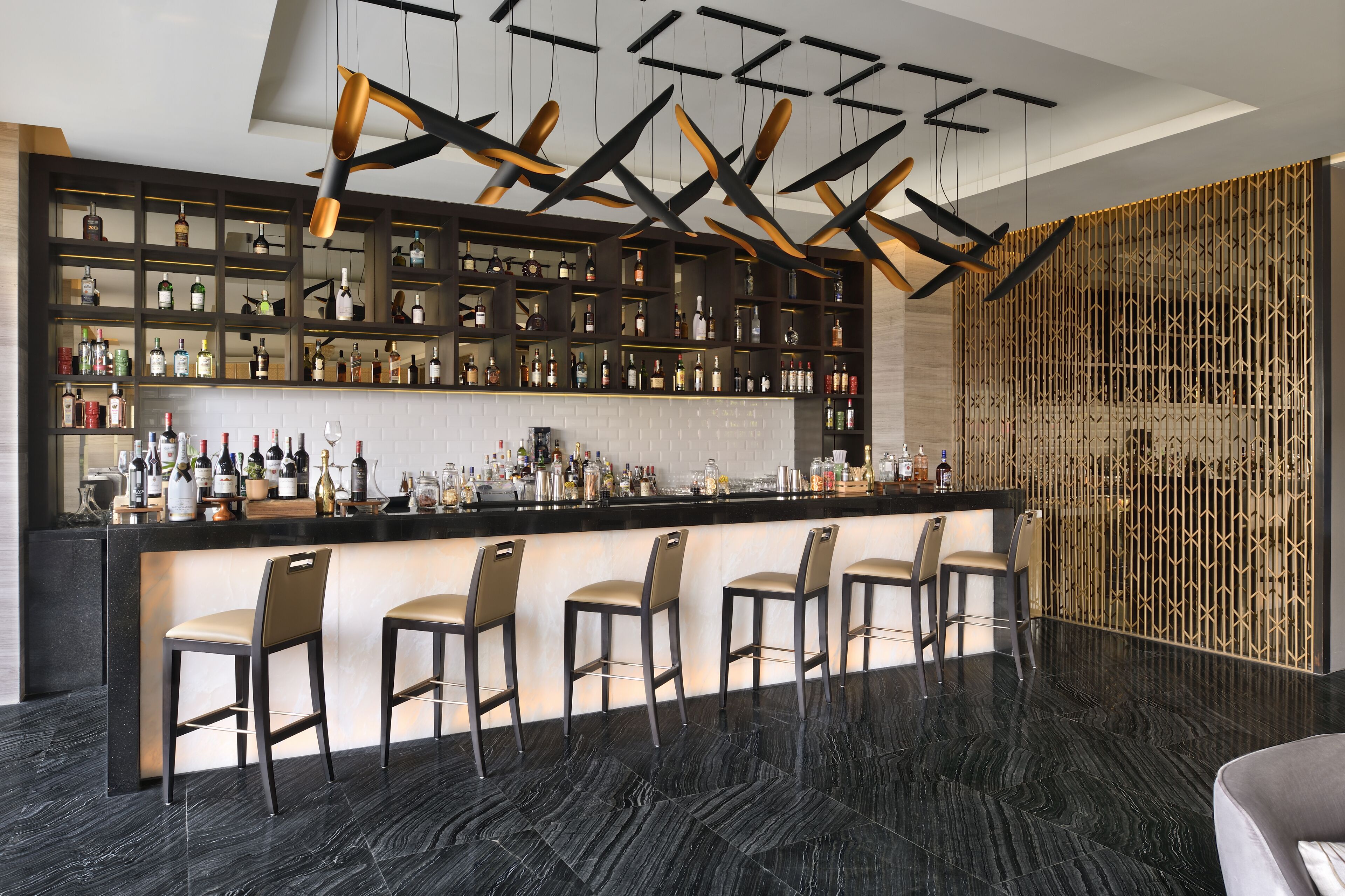A modern bar area with a black marble floor, a central bar counter, and a row of bar stools.