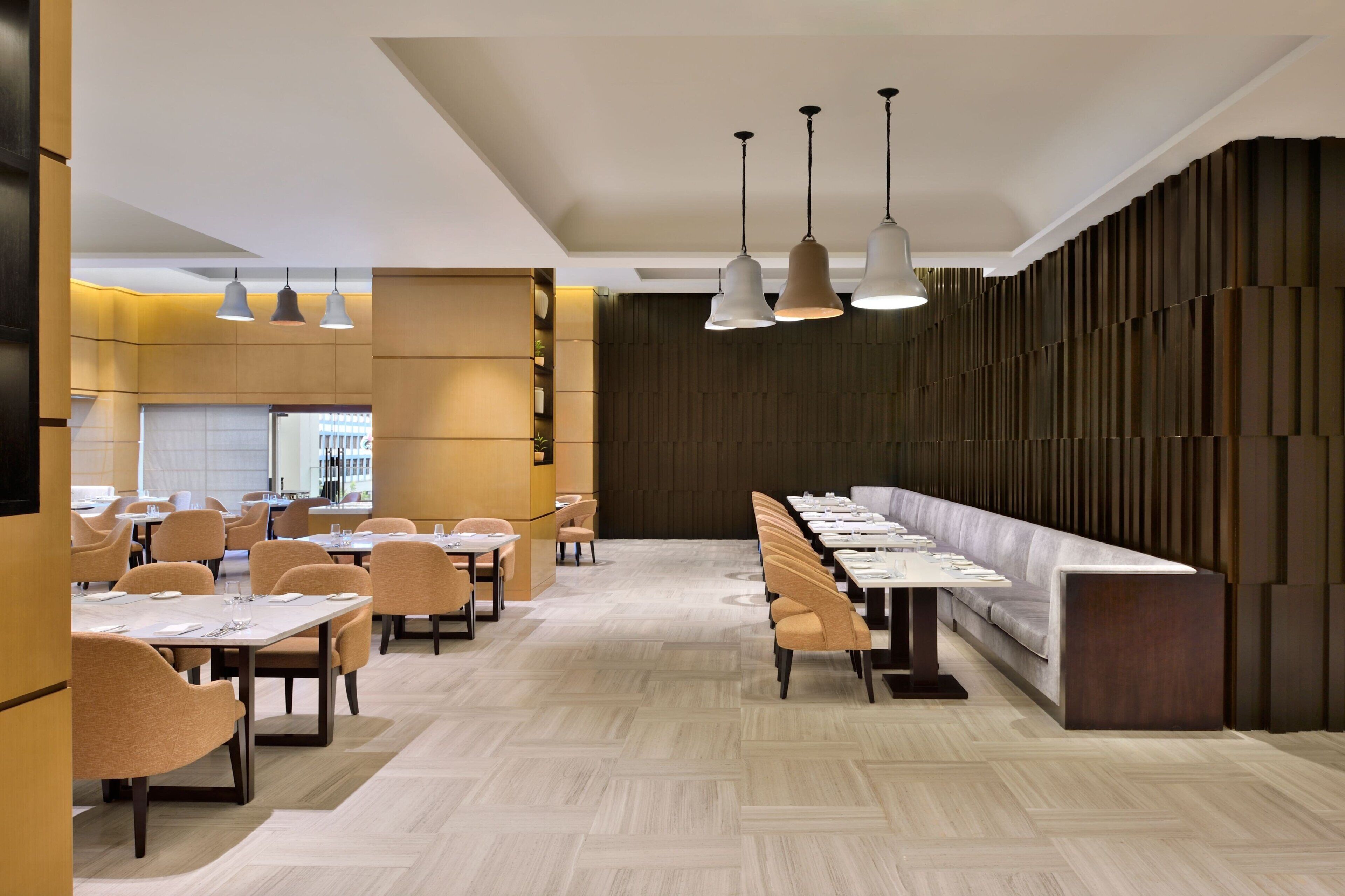 A modern restaurant interior with a long communal dining table, individual tables, and chairs.