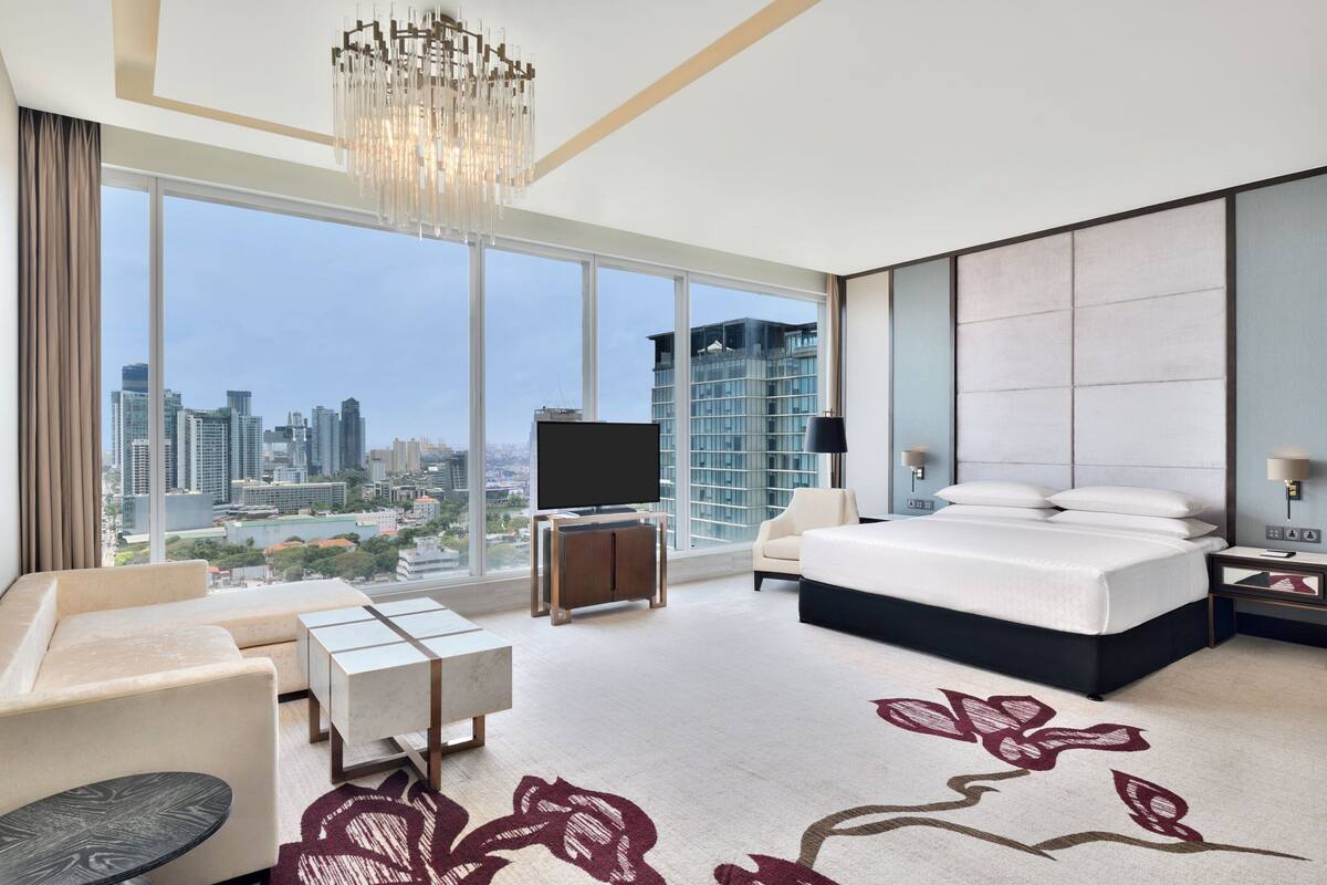 Una habitación de hotel moderna con una cama grande, un televisor, un sofá, una mesa de centro y vistas a la ciudad.