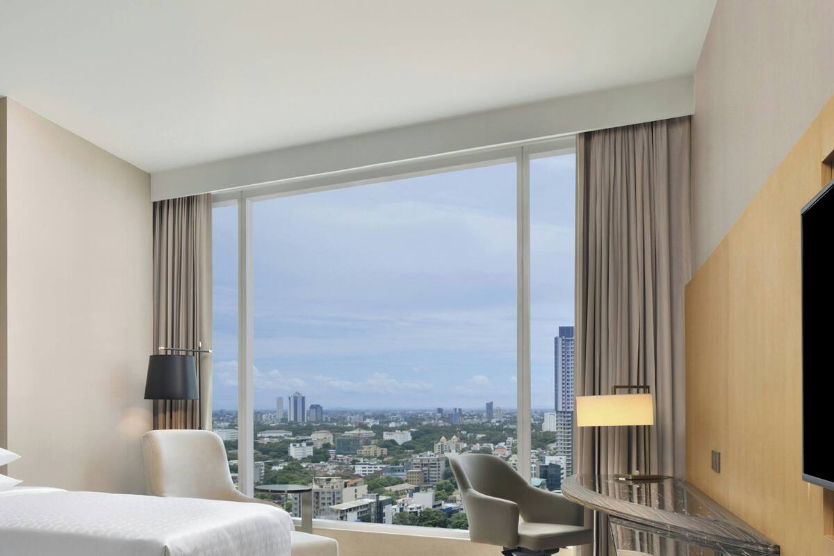Habitación de hotel con una ventana grande, cama, silla, escritorio y televisor de pantalla plana.