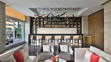 A modern lounge area with sofas, a bar with shelves of bottles, and a unique ceiling light fixture.