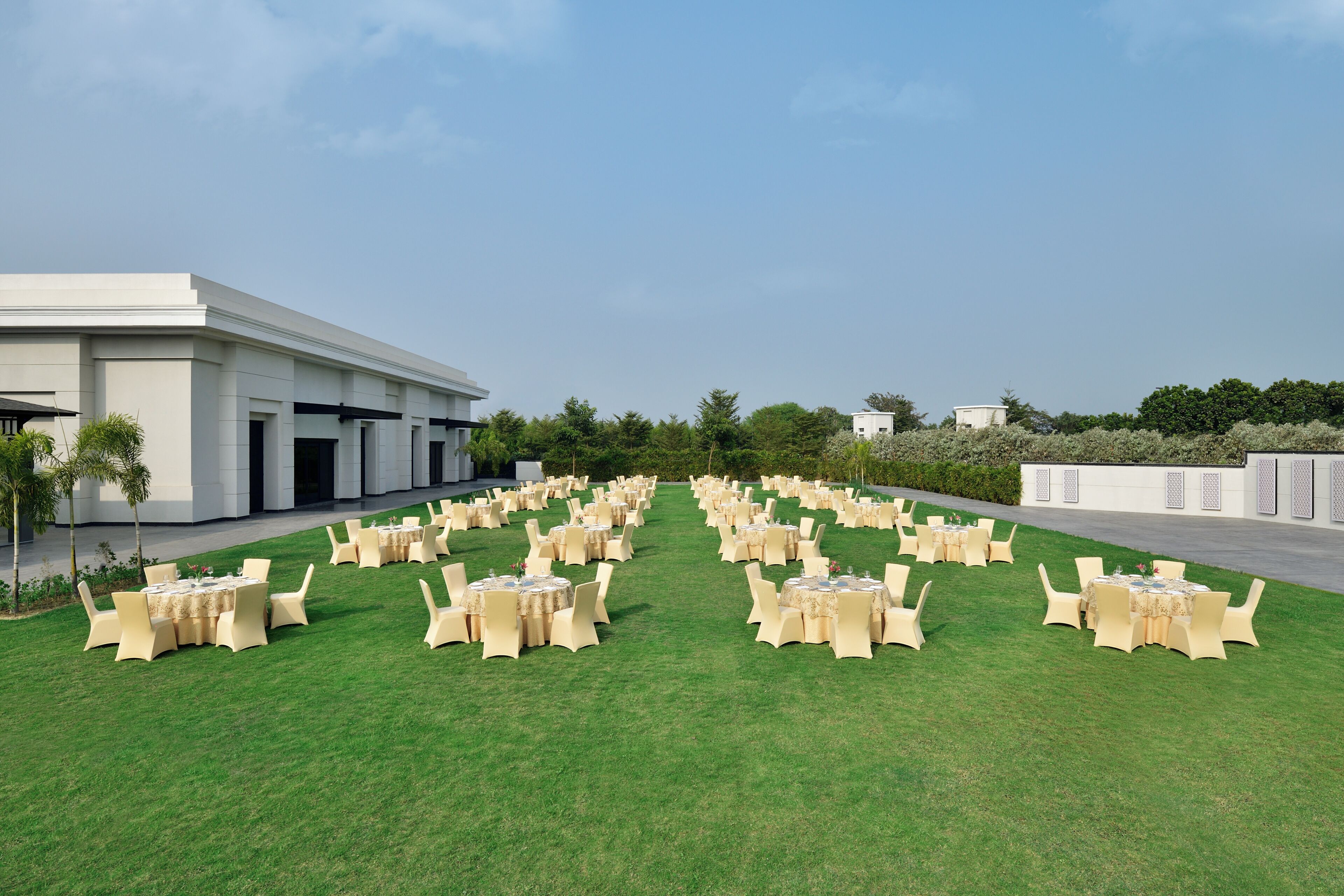 A spacious outdoor area with neatly arranged round tables and chairs, a modern building in the background, and a well-maintained lawn.