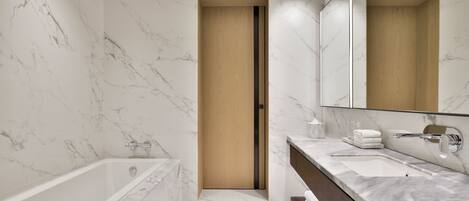 Un baño moderno con pared de mármol, puerta de madera, bañera, lavamanos y espejo.