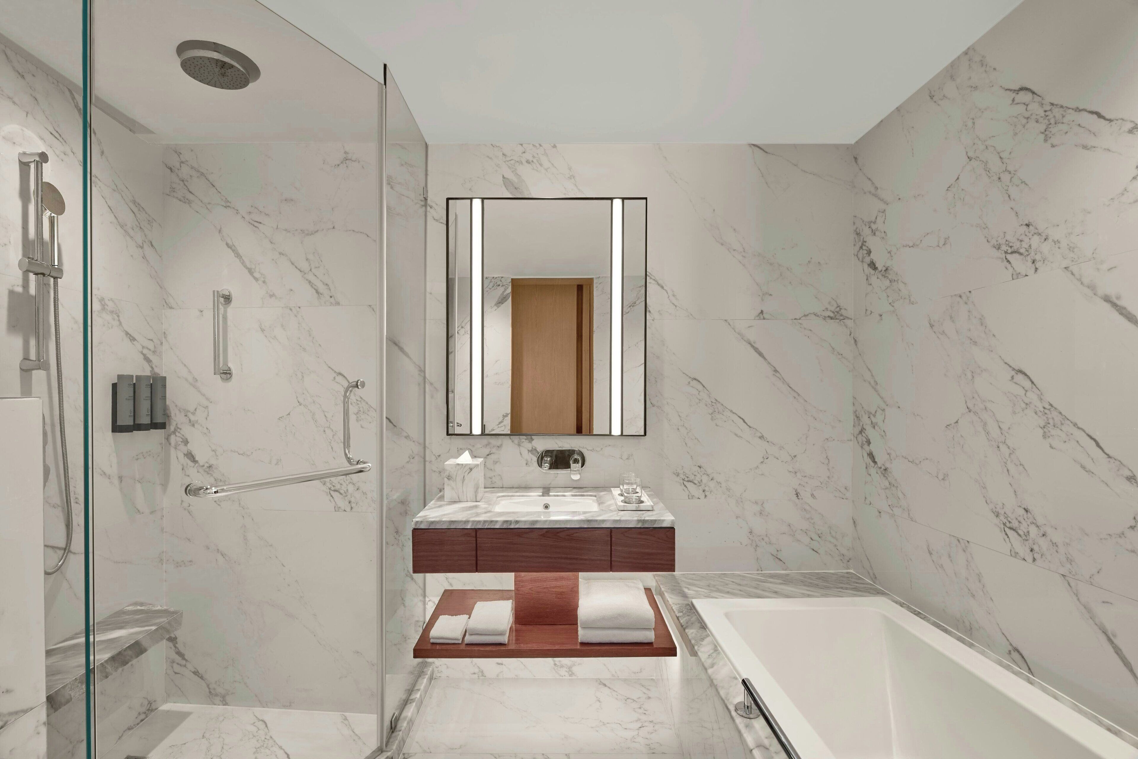 Un baño moderno con suelo de mármol, cabina de ducha de vidrio, tocador de madera, espejo grande y bañera.