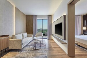 Ein modernes Hotelzimmer mit einer Sitzecke, einem kleinen runden Tisch, einem Fernseher und einem Balkon mit Aussicht.