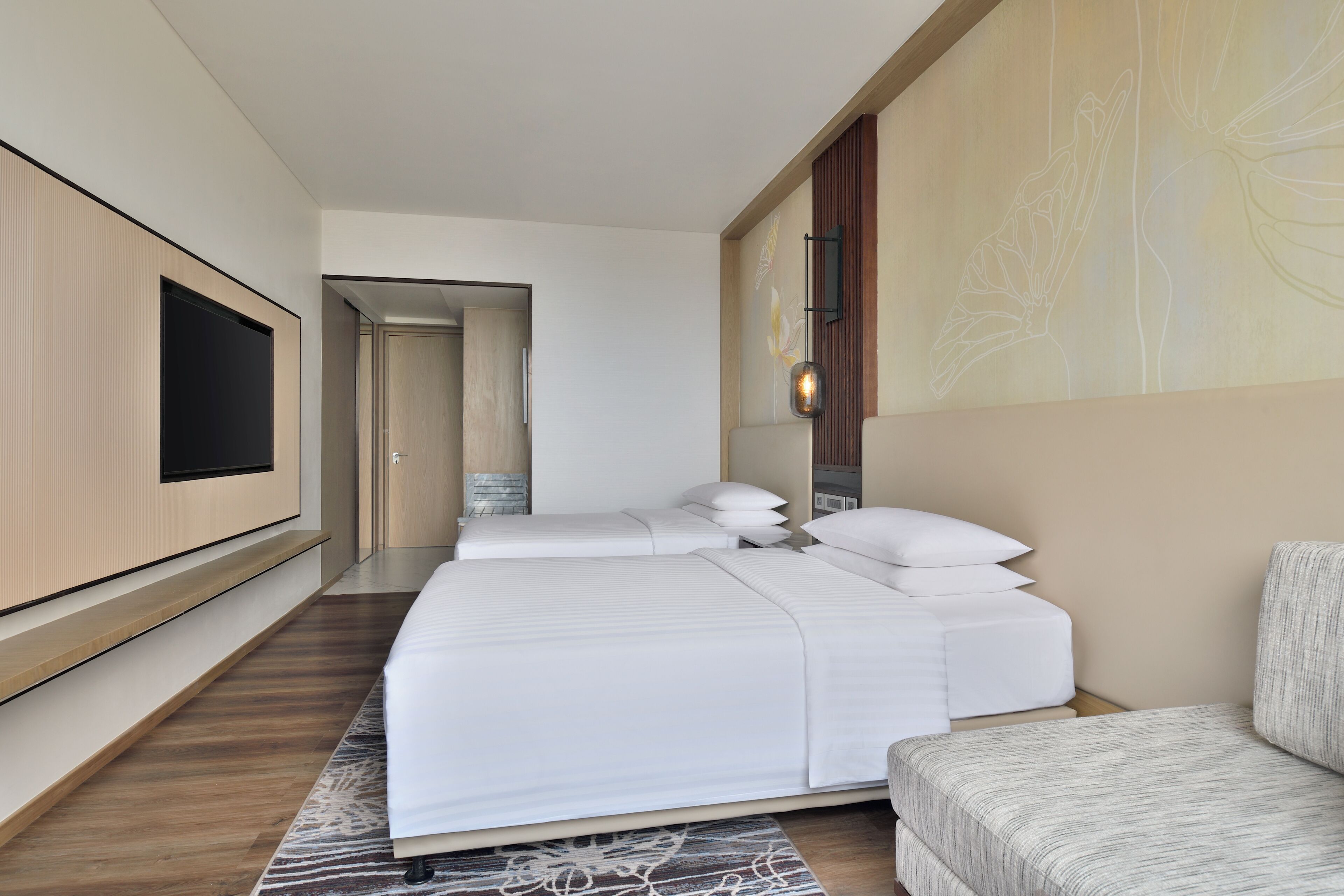 A modern hotel room with a large bed, a flat-screen TV, a seating area, and a decorative wall.