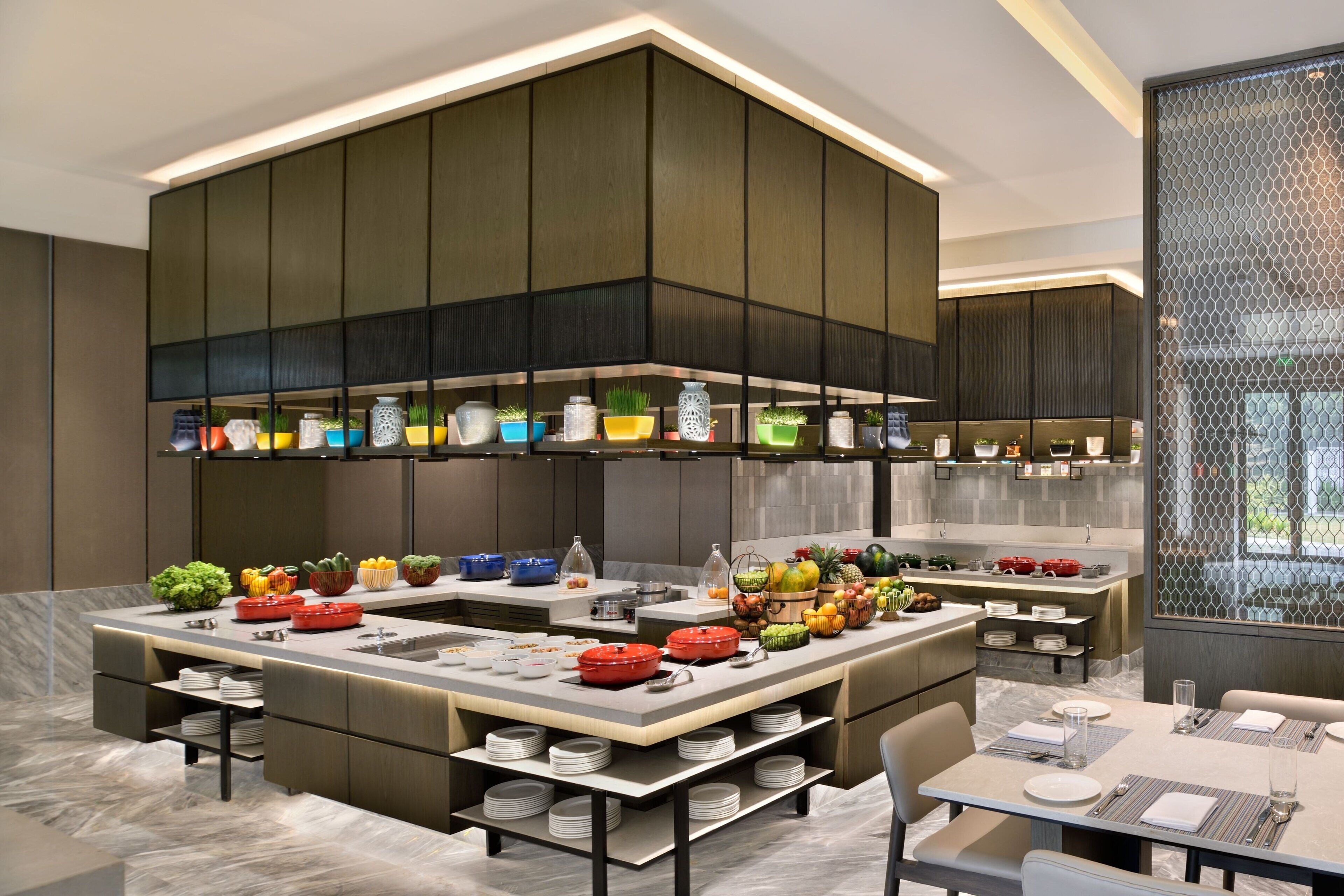 A modern kitchen with a central island, built-in appliances, and a variety of colorful plants.