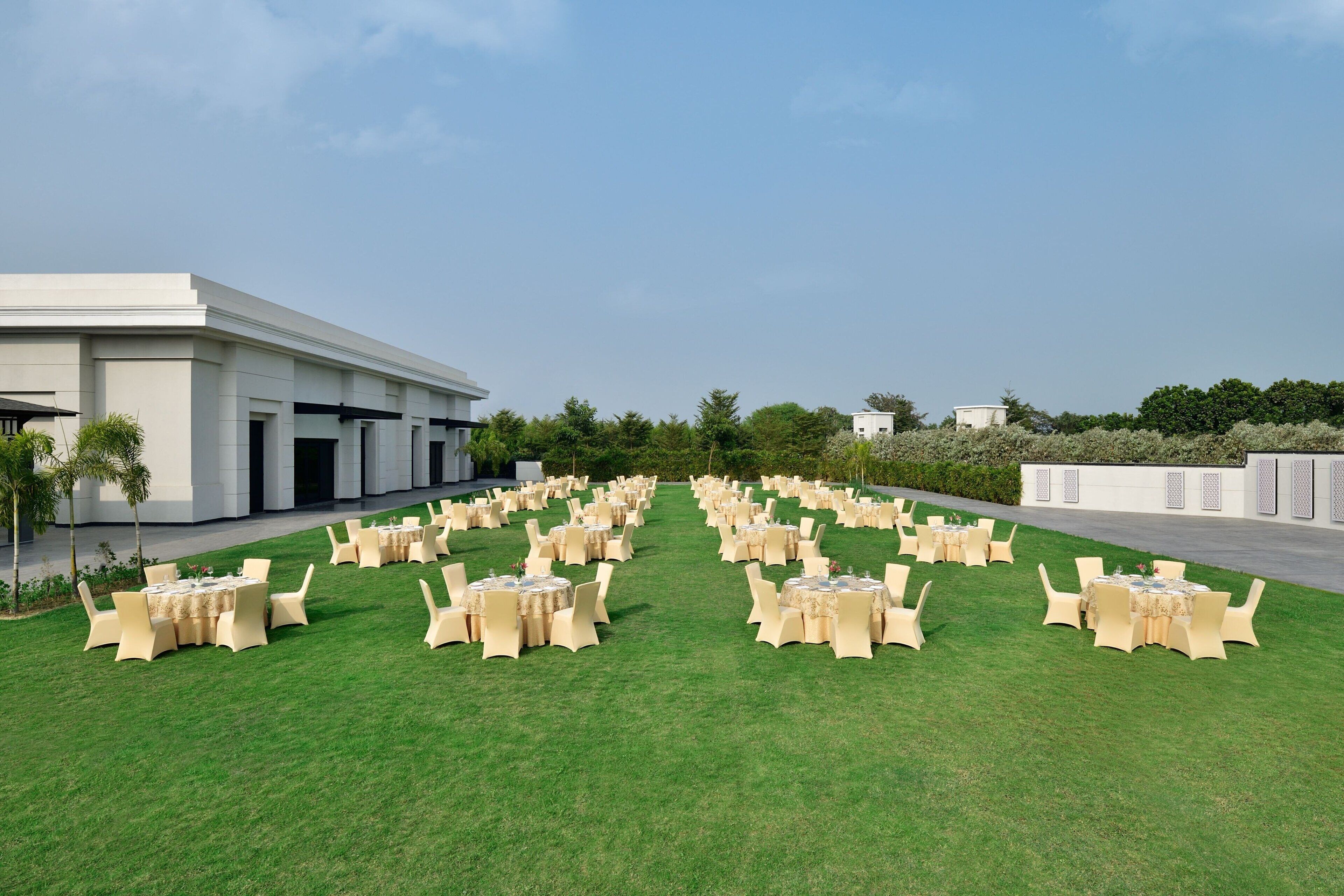 An outdoor seating area with round tables and chairs, arranged in rows on a grassy lawn, with a building in the background.