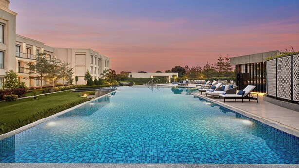 A swimming pool with lounge chairs and a building in the background. - Courtyard by Marriott Gorakhpur (Gorakhpur)