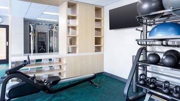 A gym with exercise equipment, a mirrored wall, and a rack of dumbbells.