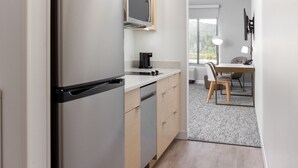 A modern kitchen with a built-in refrigerator, microwave, and coffee maker. There is a dining area with a table and chairs, and a large window providing a view of the outdoors. - TownePlace Suites by Marriott Pleasanton (Pleasanton)