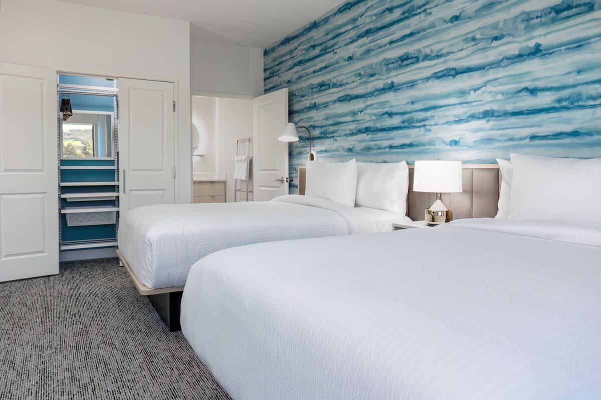 A hotel room with two beds, a large window, a wardrobe, and a blue textured wall.