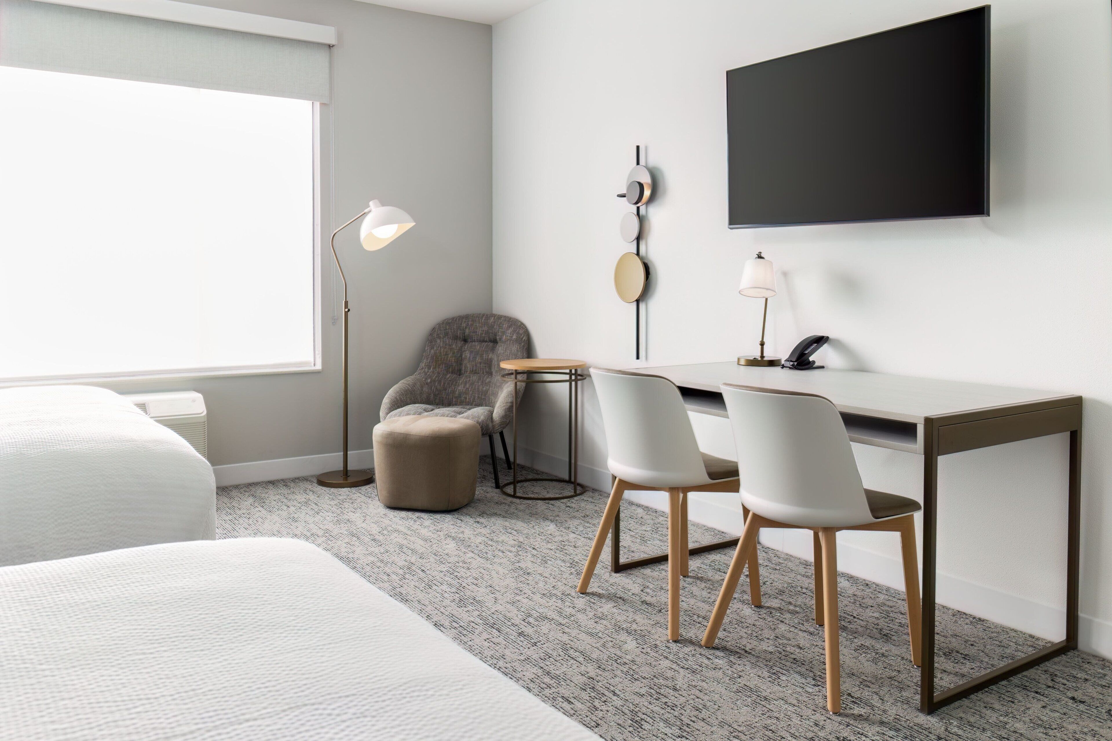 Een moderne hotelkamer met een bed, een bureau met twee stoelen, een televisie en een lamp.