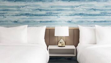 Camera d'albergo con due letti, un comodino con una lampada e una parete decorata con un motivo astratto blu.