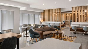 Een moderne hotel lobby met een zithoek, tafels en een decoratieve houten scheiding.