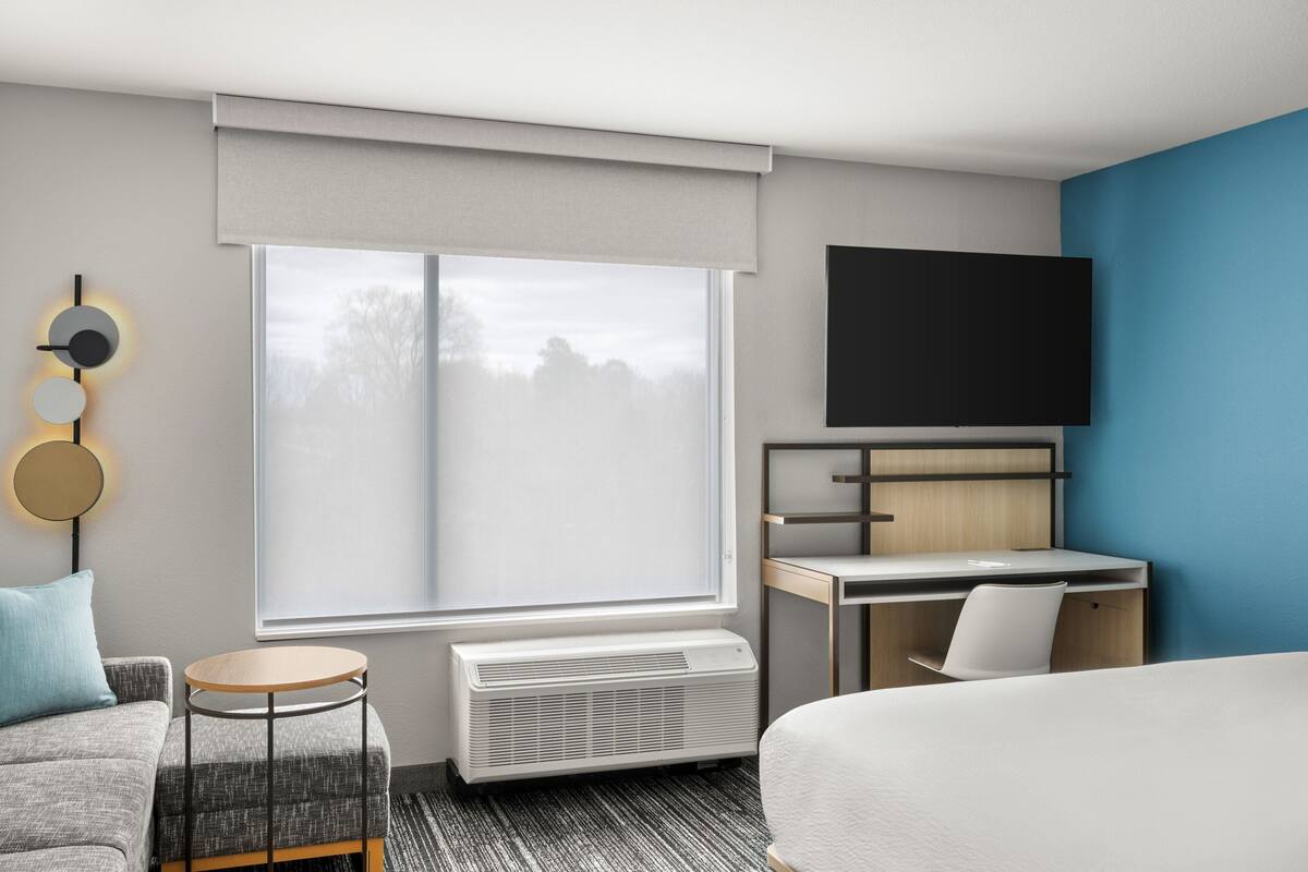 Une chambre d’hôtel moderne dotée d’une grande fenêtre, d’un téléviseur à écran plat, d’un bureau, d’un lit et d’une petite table ronde.