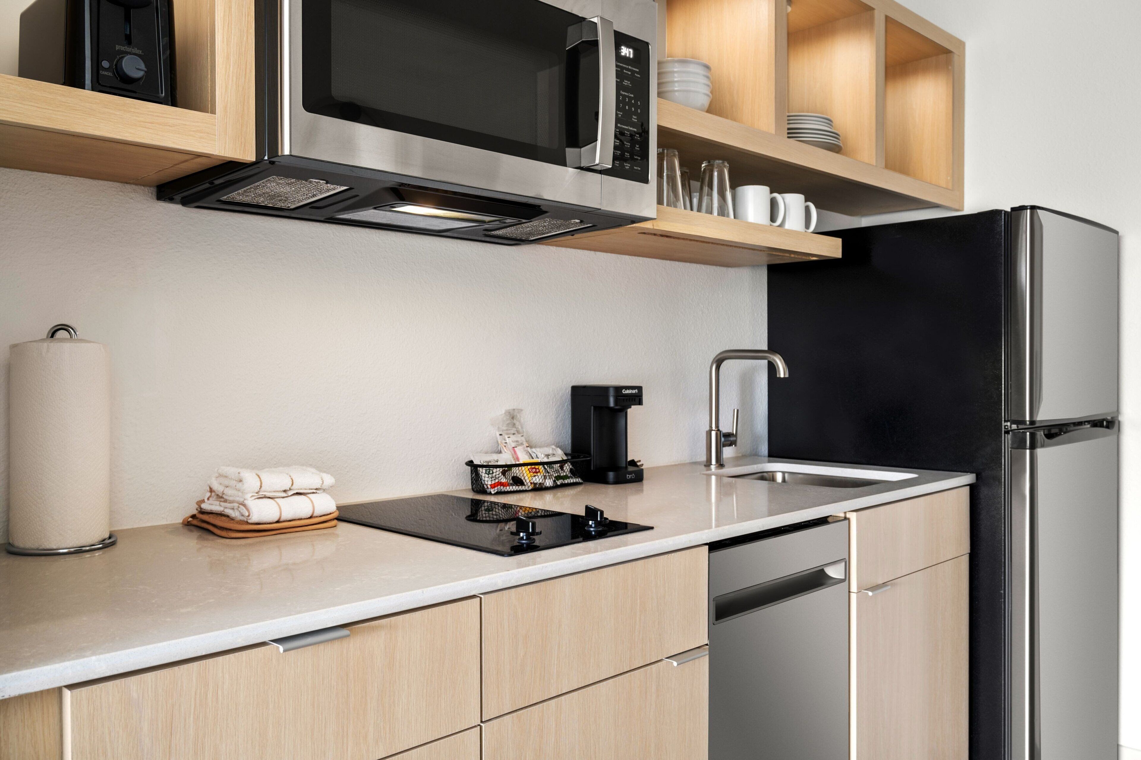 A modern kitchen with a stainless steel refrigerator, a built-in microwave, and a coffee maker.