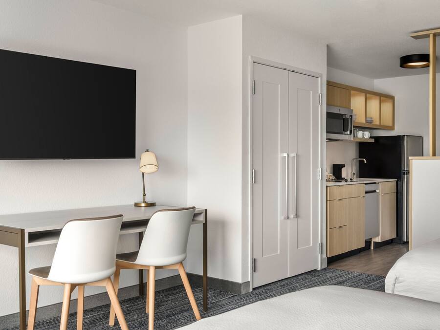 Een moderne hotelkamer met een bureau, twee stoelen, een bed, een kledingkast en een kitchenette.