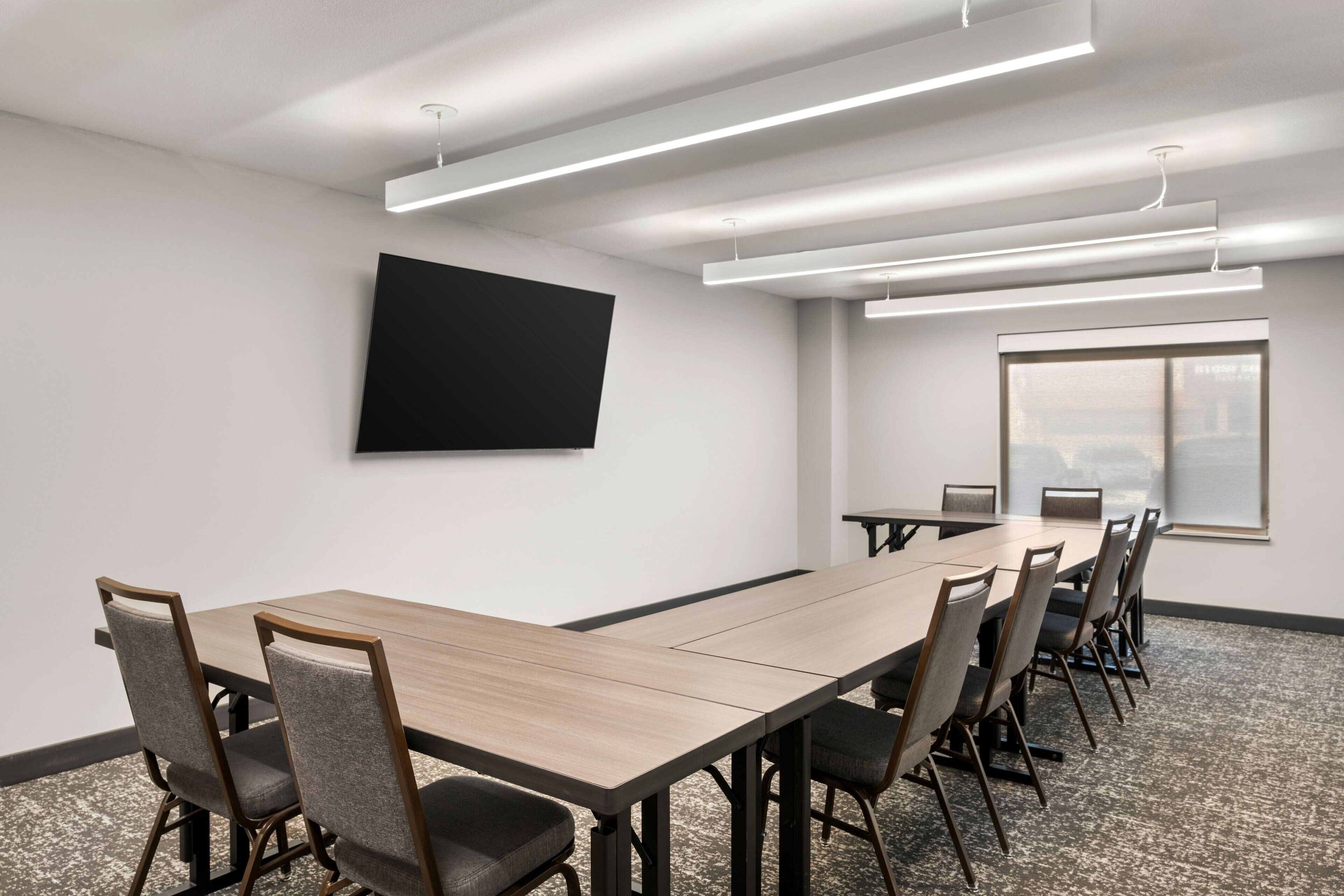 A conference room with a long table, chairs, a flat-screen TV, and a large window.