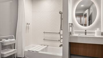 A modern bathroom with a white bathtub, a shower, a vanity with a mirror, and a towel rack.
