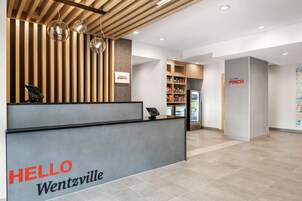 Uma área de recepção com uma placa 'HELLO Wentzville', um balcão de recepção, uma placa 'BONVOY', uma placa 'PINCH' e uma geladeira com bebidas.