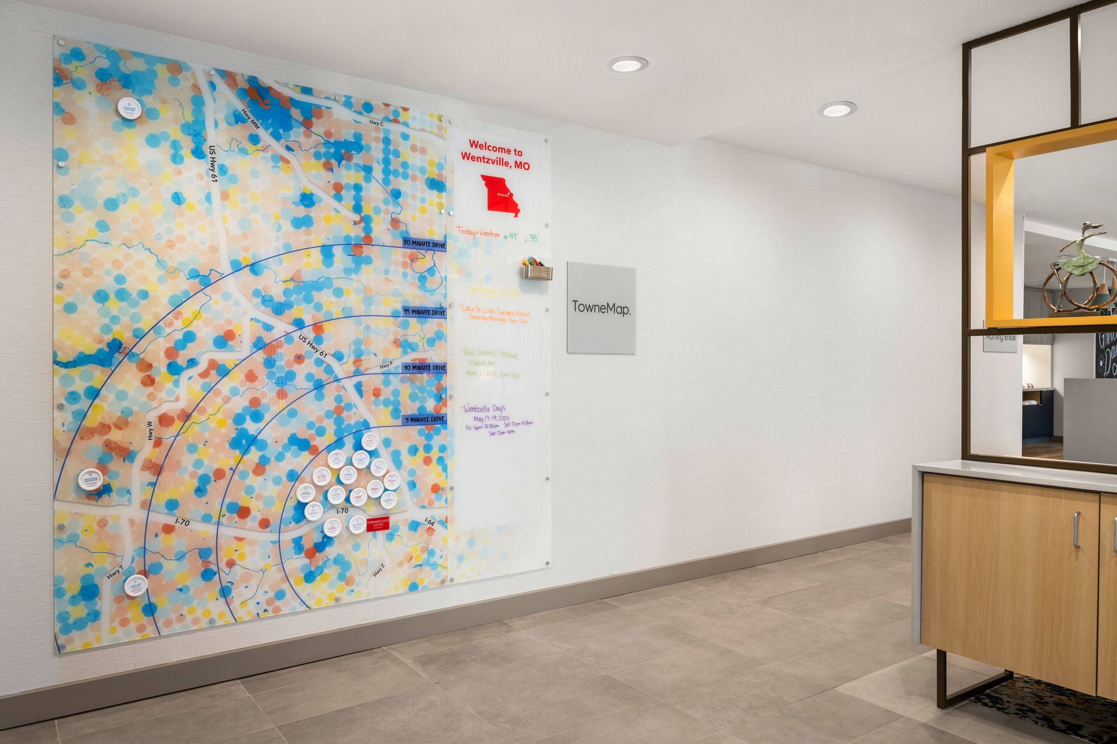 A hallway with a large colorful map on the wall, a sign reading "Welcome to Wentzville, MO," and a cabinet with a mirror.