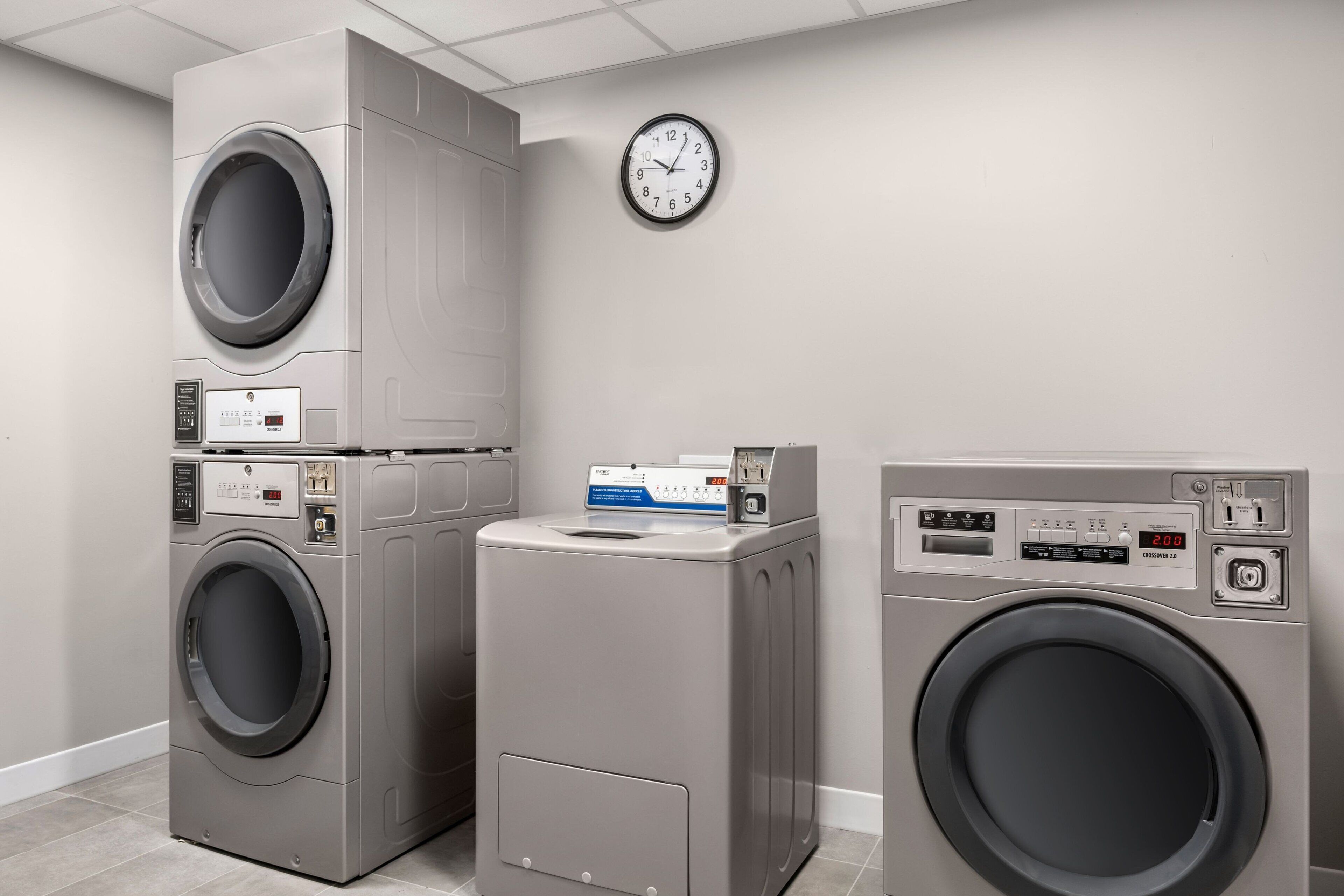 A laundry room with three stacked washing machines, a clock on the wall, and a digital display on one machine.