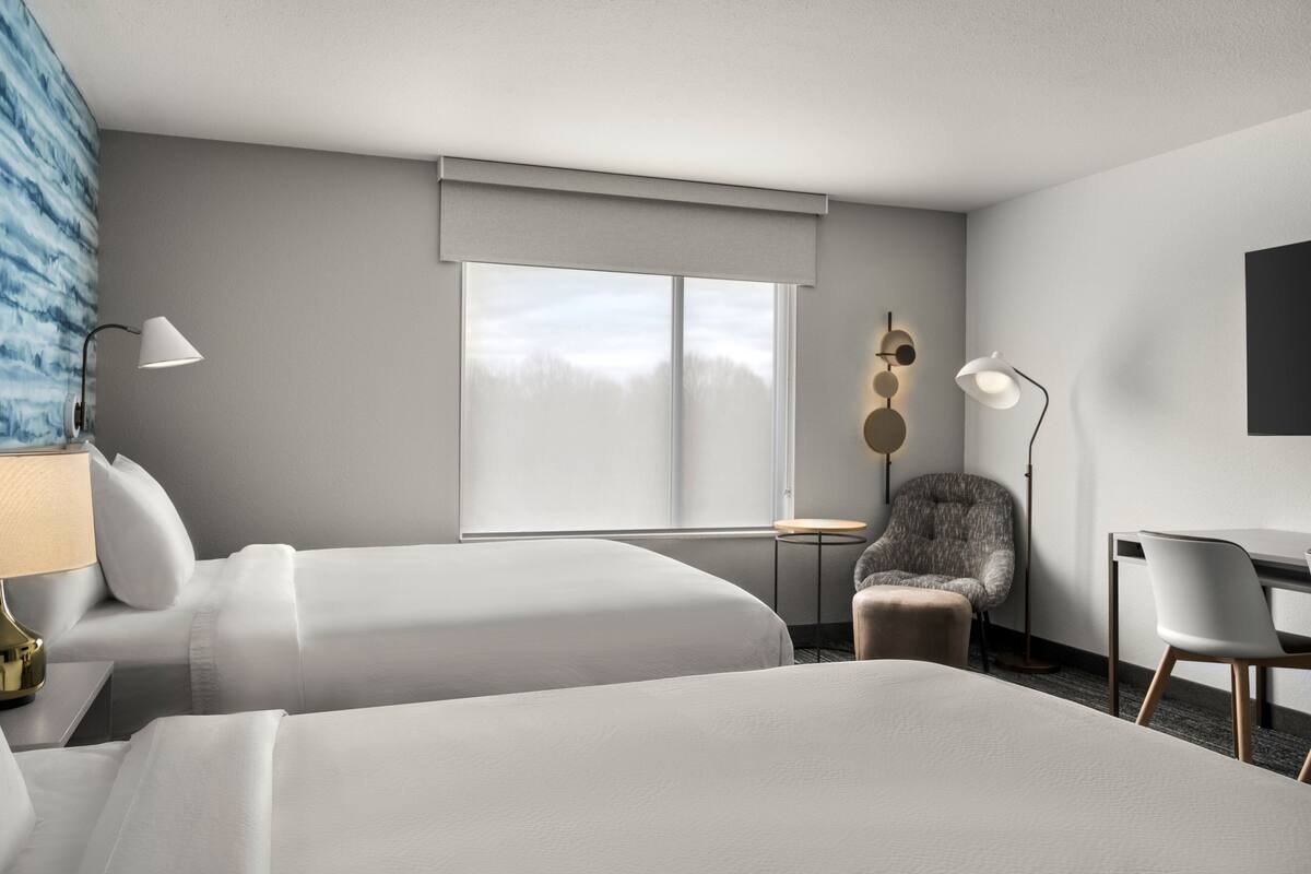 Une chambre d’hôtel avec deux lits, un bureau, une chaise, une lampe et une vue sur l’extérieur.