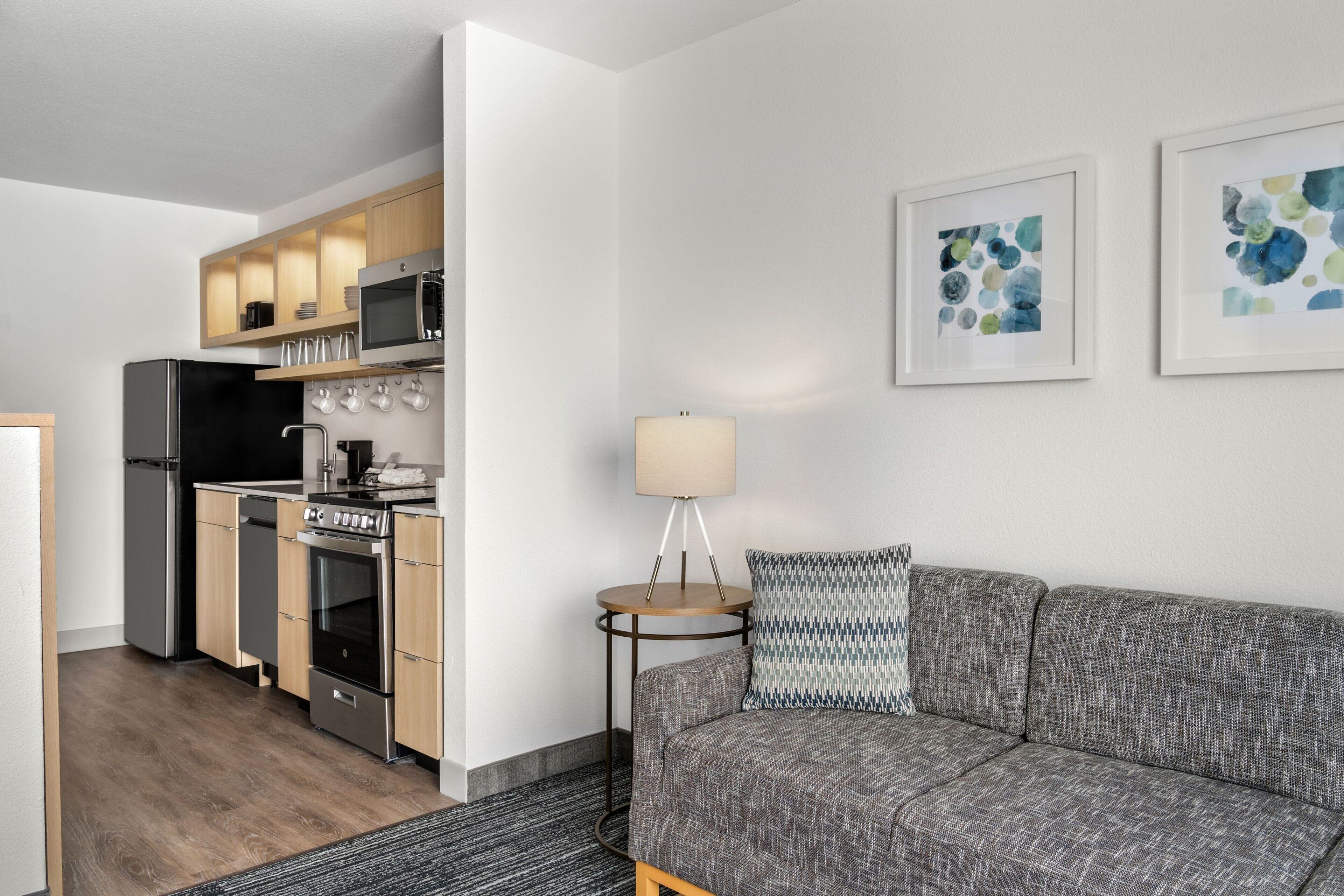 A modern kitchen with stainless steel appliances, a gray sofa, and two framed abstract paintings.