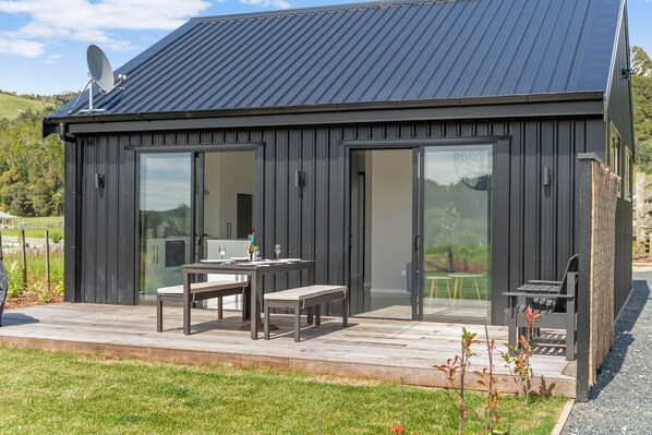 Um edifício moderno de cor escura, com telhado de metal, grandes portas de vidro e um espaço de terraço com mesa e cadeiras.