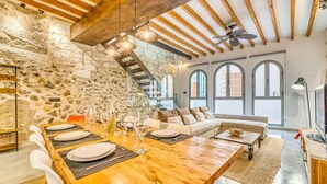 Ein rustikaler Essbereich mit einem Holztisch, gedeckt für sechs Personen, einer Steinwand und einer Loggia-Decke mit freiliegenden Balken.