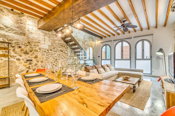 A rustic dining area with a wooden table set for six, a stone wall, and a loft-style ceiling with exposed beams.