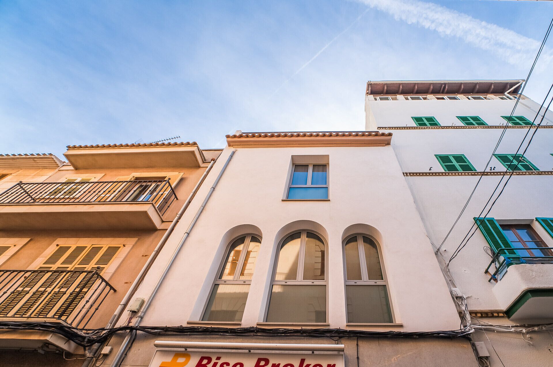 A building with a visible storefront labeled 'Riso Broker' and a balcony with a metal railing.