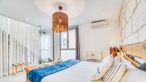 Ein modernes Schlafzimmer mit einem großen Bett, einem Nachttisch aus Holz, einer Hängeleuchte und Blick ins Freie durch ein Fenster.