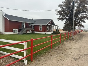 A red building with a white porch and a red fence in front. - Adorable Farmhouse within steps of Double Check Arena! (Eaton)