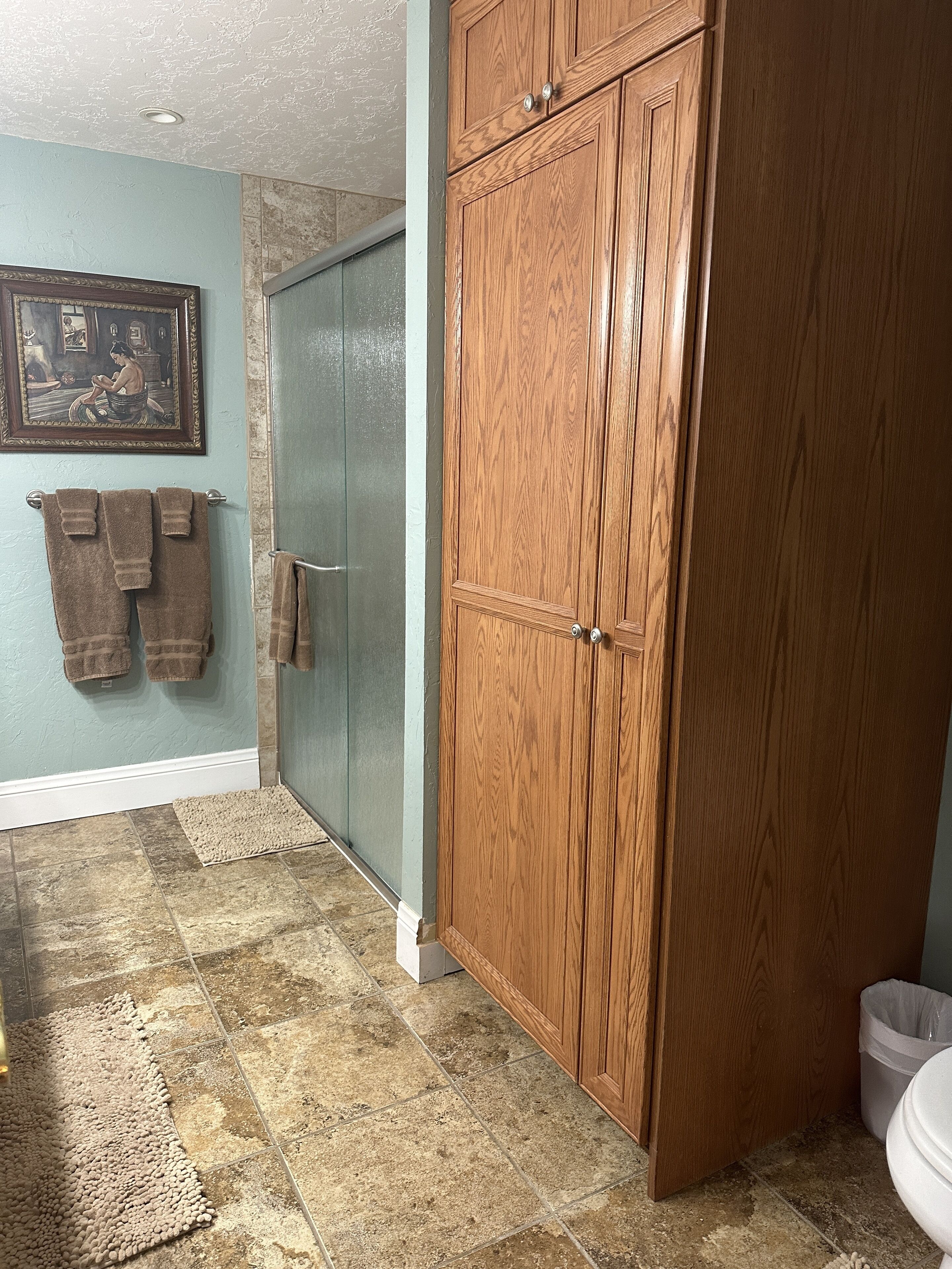 Une salle de bain avec un placard en bois, une cabine de douche en verre et un carrelage au sol.