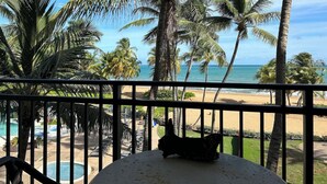 A balcony with a view of a beach, palm trees, and a pool. - Resort Condo at Wyndham Grand Rio Mar (Río Grande)