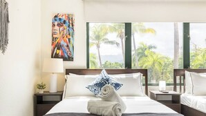A hotel room with a bed, a painting, a nightstand, a lamp, and a view of palm trees. - Resort Condo at Wyndham Grand Rio Mar (Río Grande)